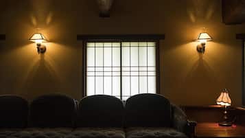 A dimly lit room with a sofa, two wall-mounted lamps, and a window with a grid pattern.