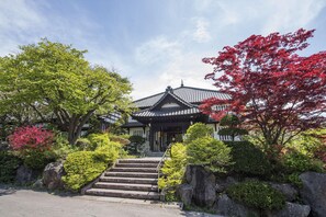 A traditional Japanese building with a tiled roof, surrounded by lush greenery and a stone staircase leading to the entrance. - Ginrinsou (Otaru)