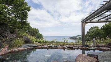 A tranquil outdoor setting with a clear view of the sea, a stone pathway, and a wooden pergola.
