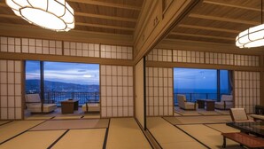 A traditional Japanese-style room with tatami flooring, sliding shoji doors, and a view of the cityscape at dusk.