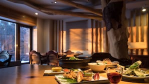 A dining table with various dishes, a bowl, and a glass of red wine in a restaurant with a modern interior and large windows. - Hotel Daiheigen (Otofuke)