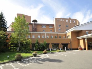 A hotel with a brick facade, multiple windows, and a parking lot with marked spaces. - Hotel Daiheigen (Otofuke)