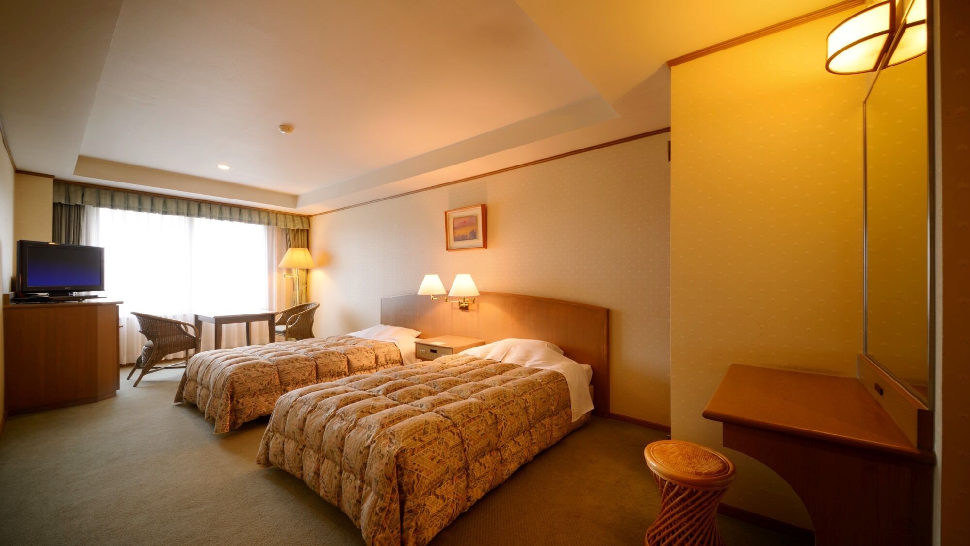 A hotel room with two beds, a desk with a television, a chair, and a lamp.