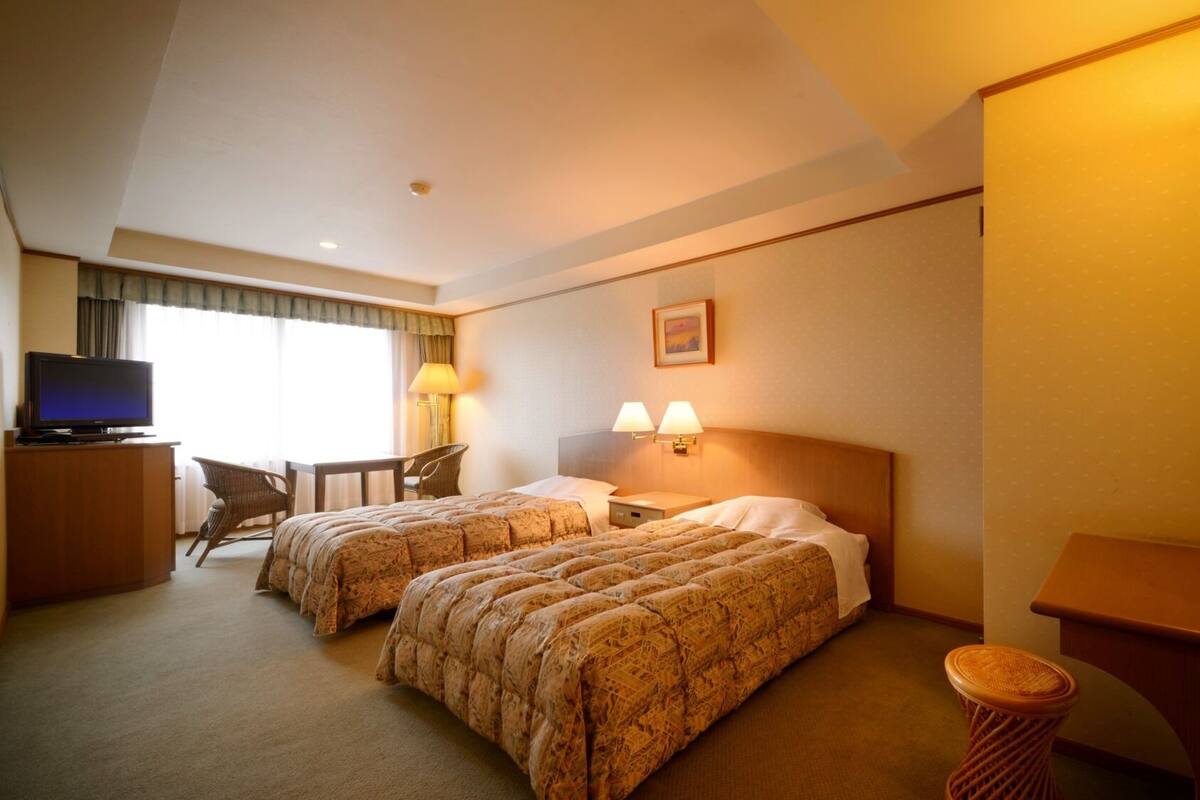 A hotel room with two beds, a desk with a television, a chair, and a lamp.