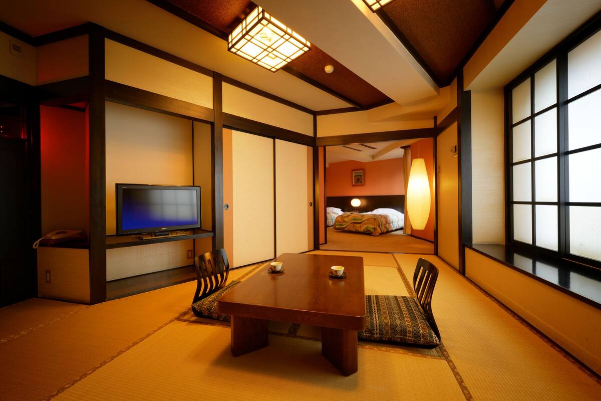 A traditional Japanese-style room with tatami flooring, a low wooden table, and a television.
