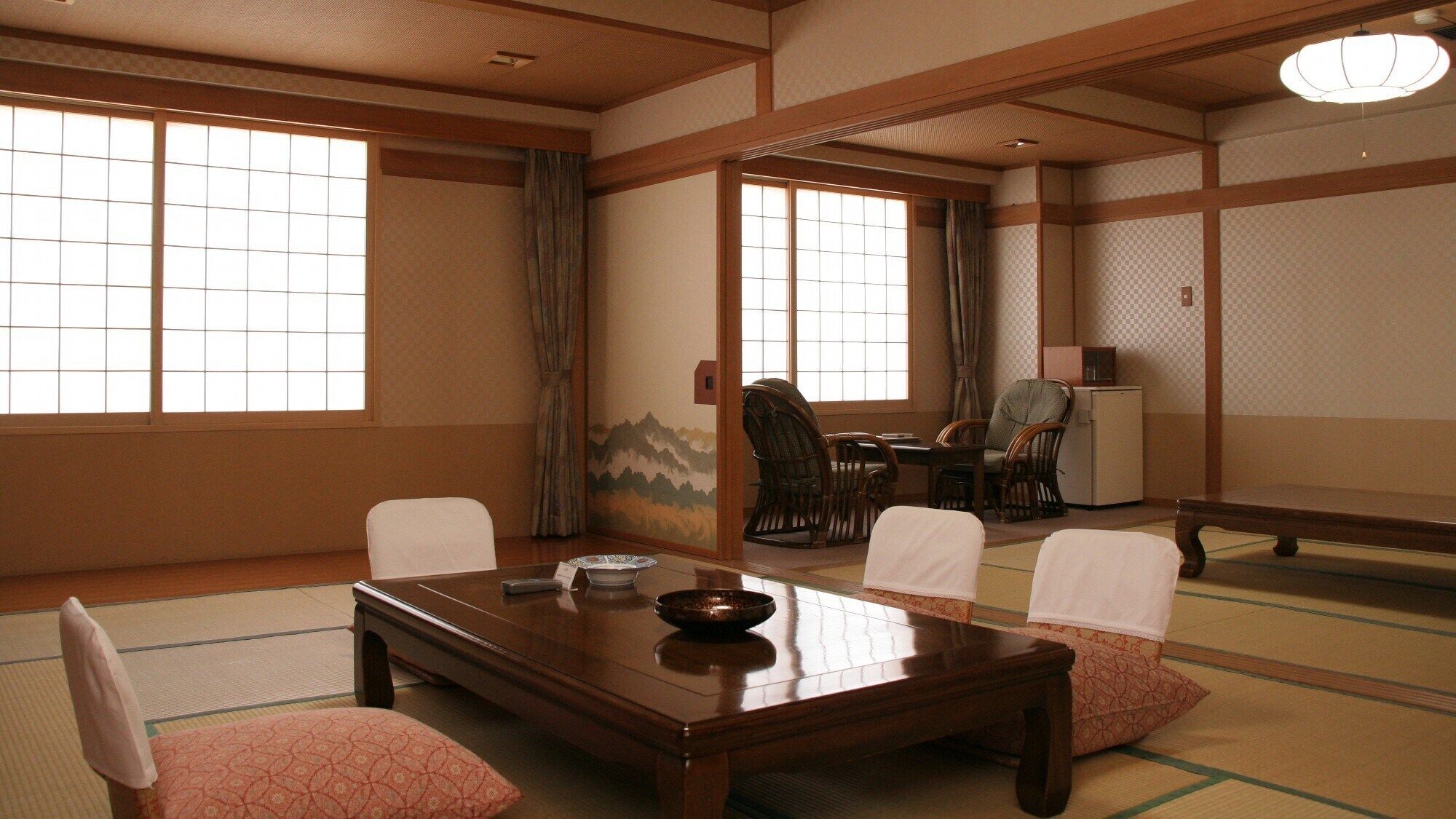 A traditional Japanese room with tatami flooring, a low table, chairs, and a view of the outside through shoji screens.