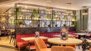 A restaurant interior with booths, round tables, and a wall adorned with plants and decorative items. - Premier Inn London Tower Bridge (London)