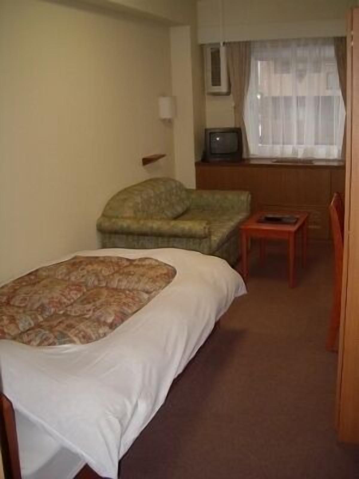 Een hotelkamer met een bed, een klein tafeltje, een stoel, een televisie en een raam met gordijnen.