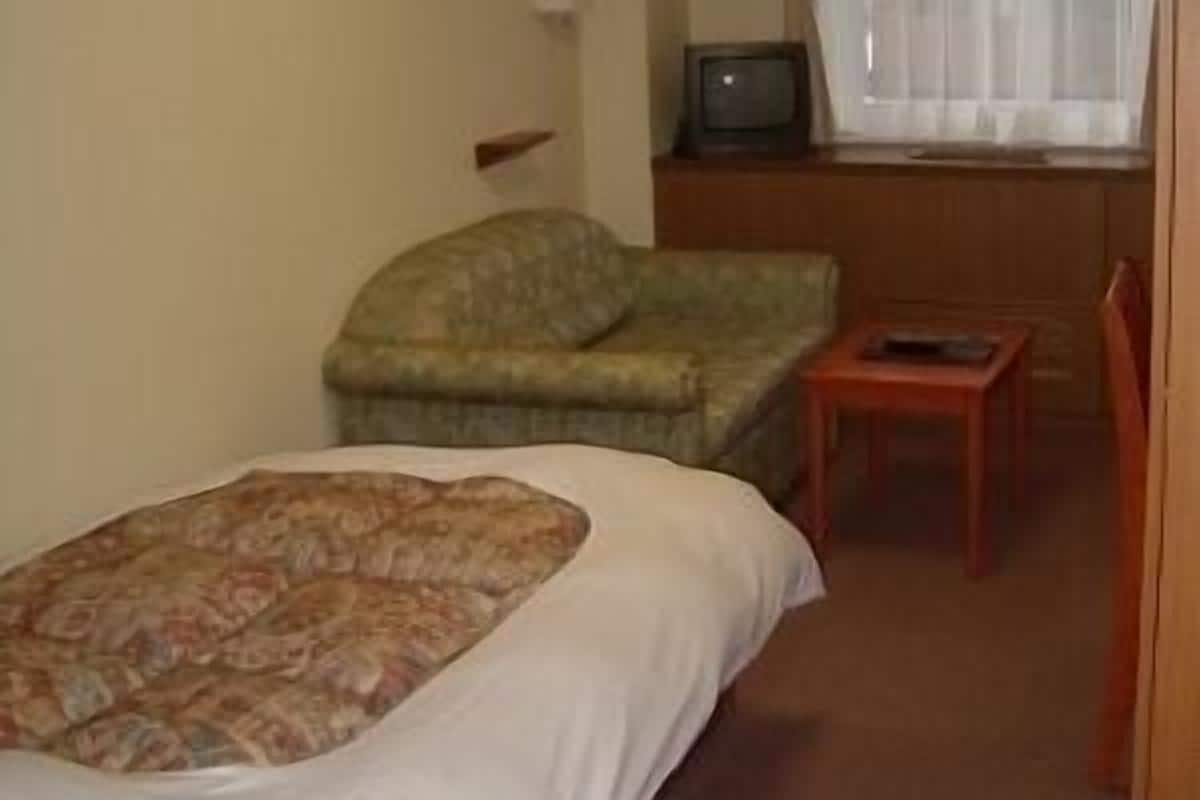 A hotel room with a bed, a small table, a chair, a television, and a window with curtains.