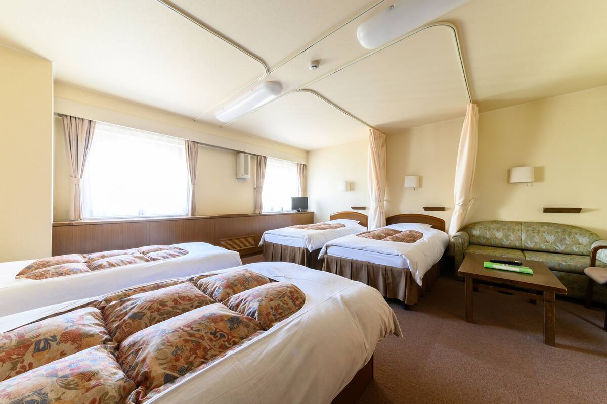 A hotel room with two beds, a sofa, a small table, and a window with curtains.