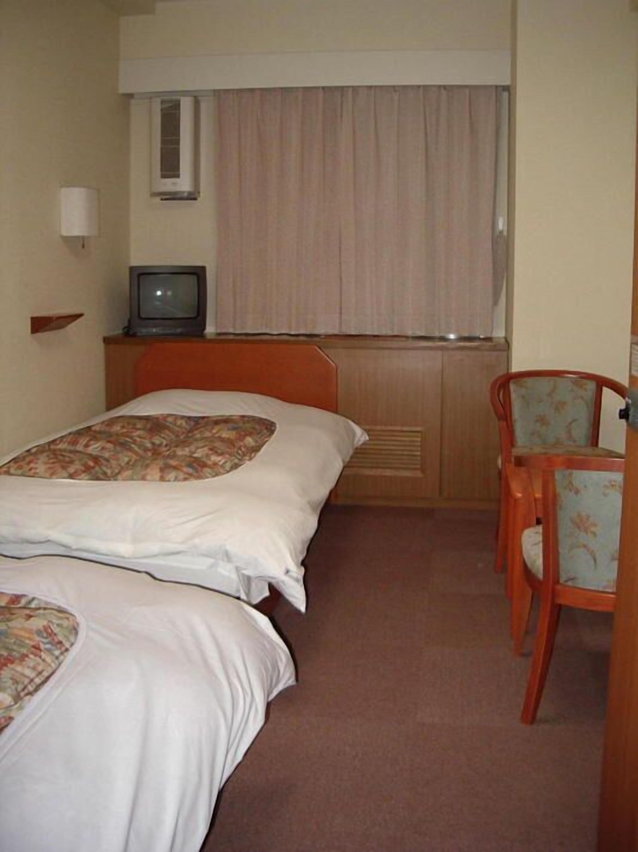 Een hotelkamer met twee bedden, een televisie, een stoel en een raam met gordijnen.