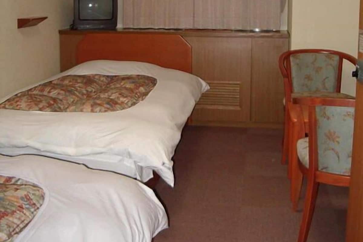 A hotel room with two beds, a television, a chair, and a window with curtains.