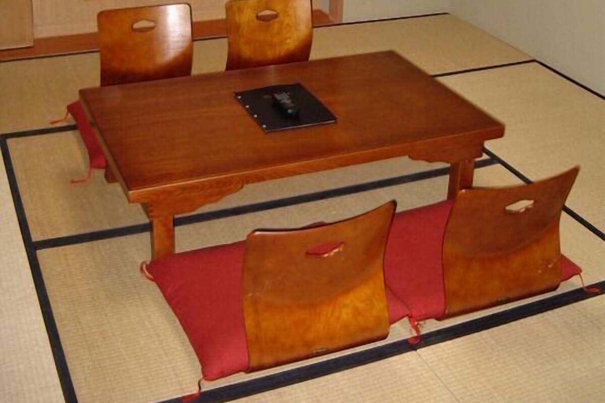 A tatami mat room with a wooden table, four chairs, and a television on a shelf.