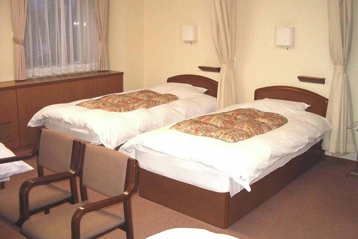 A hotel room with two single beds, a wooden headboard, a small table, and a chair.