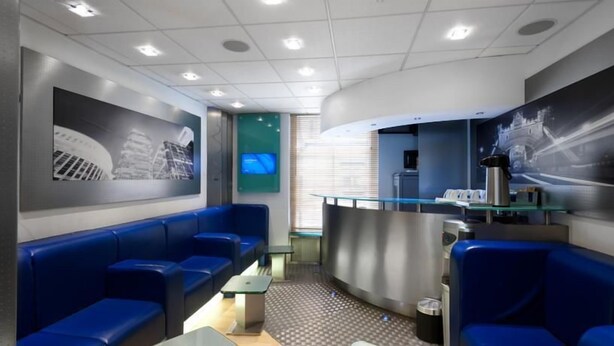 A modern waiting area with blue seating, a reception desk, and cityscape artwork on the walls.
