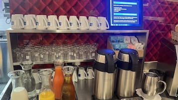 A coffee station with multiple coffee makers, a milk dispenser, and a variety of coffee cups.