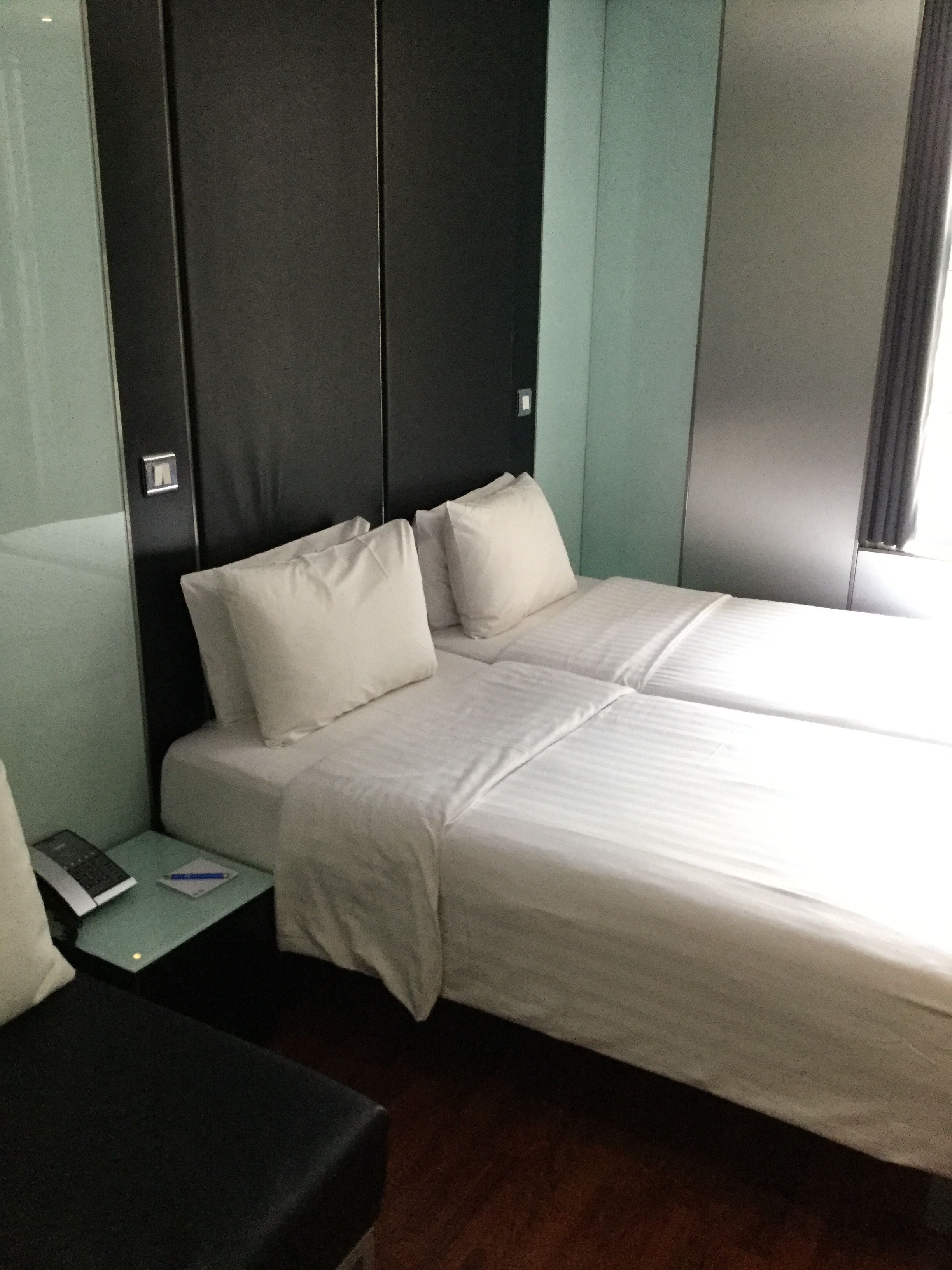 A hotel room with two beds, a small table with a book and pen, and a black chair.