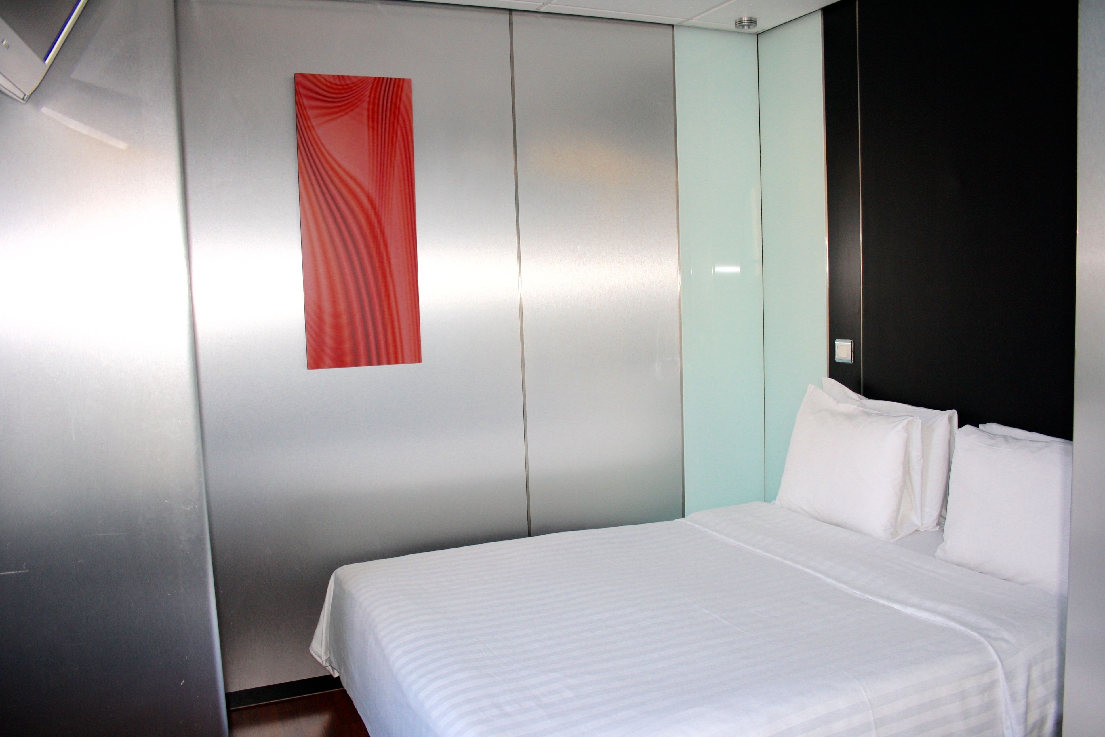 A hotel room with a bed, a red curtain, and a black headboard.