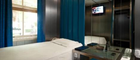 Una habitación de hotel con cama, escritorio, silla, televisor y ventana con cortinas.
