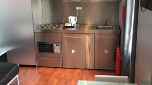 A compact kitchen with stainless steel appliances, a coffee maker, and a fire extinguisher.