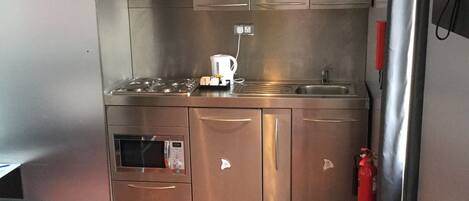 Cocina compacta con electrodomésticos de acero inoxidable, cafetera y extintor.