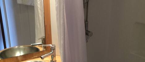 A bathroom with a wooden vanity, a stainless steel sink, and a shower curtain.
