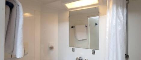 Un baño con lavamanos blanco, un espejo, una toalla colgada en la pared y una cortina de ducha.