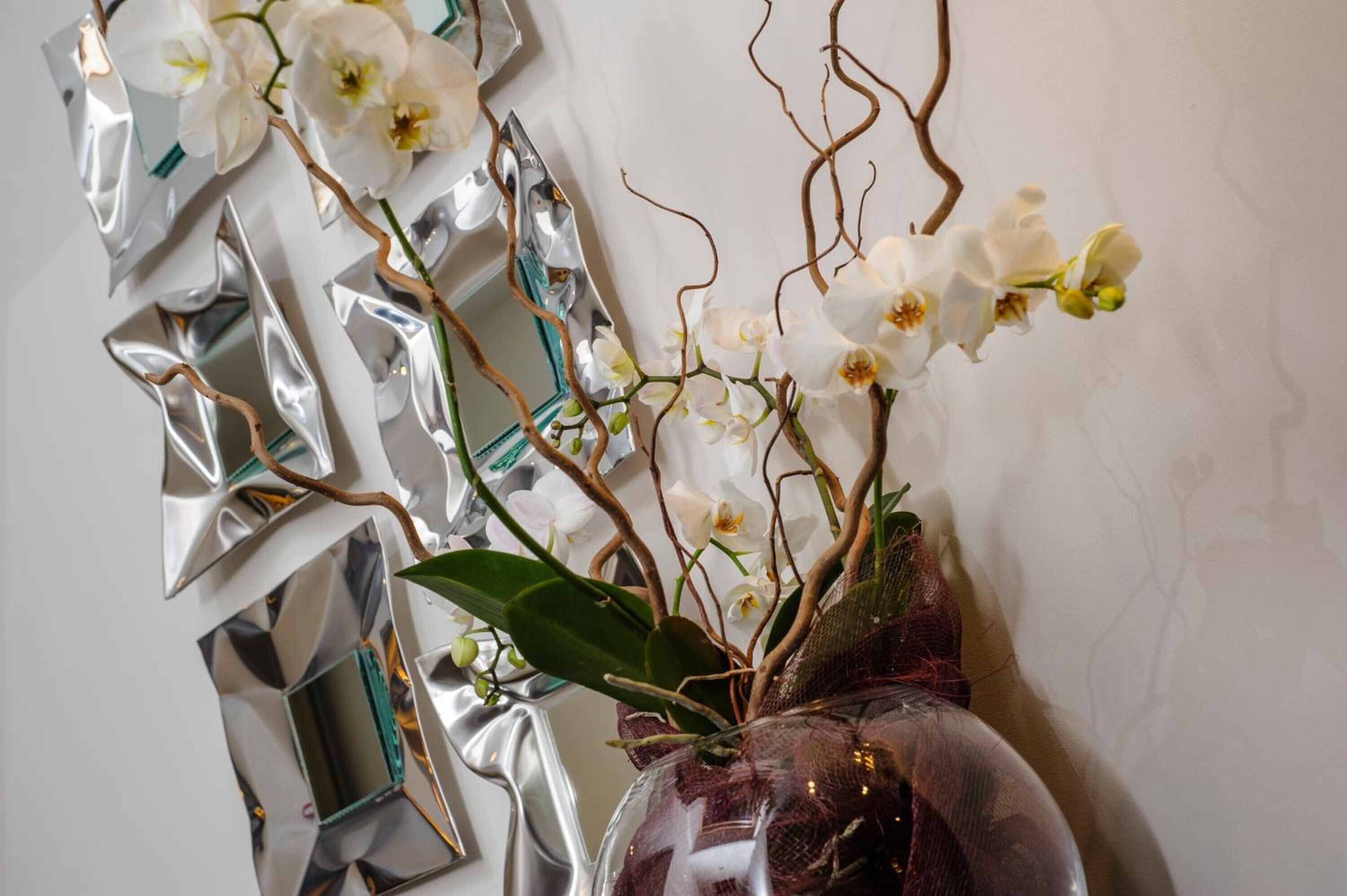 Een vaas met witte orchideeën en een spiegelende wand.