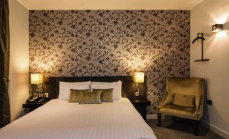 Habitación de hotel con una cama grande, dos lámparas de noche, una silla y un papel tapiz estampado.