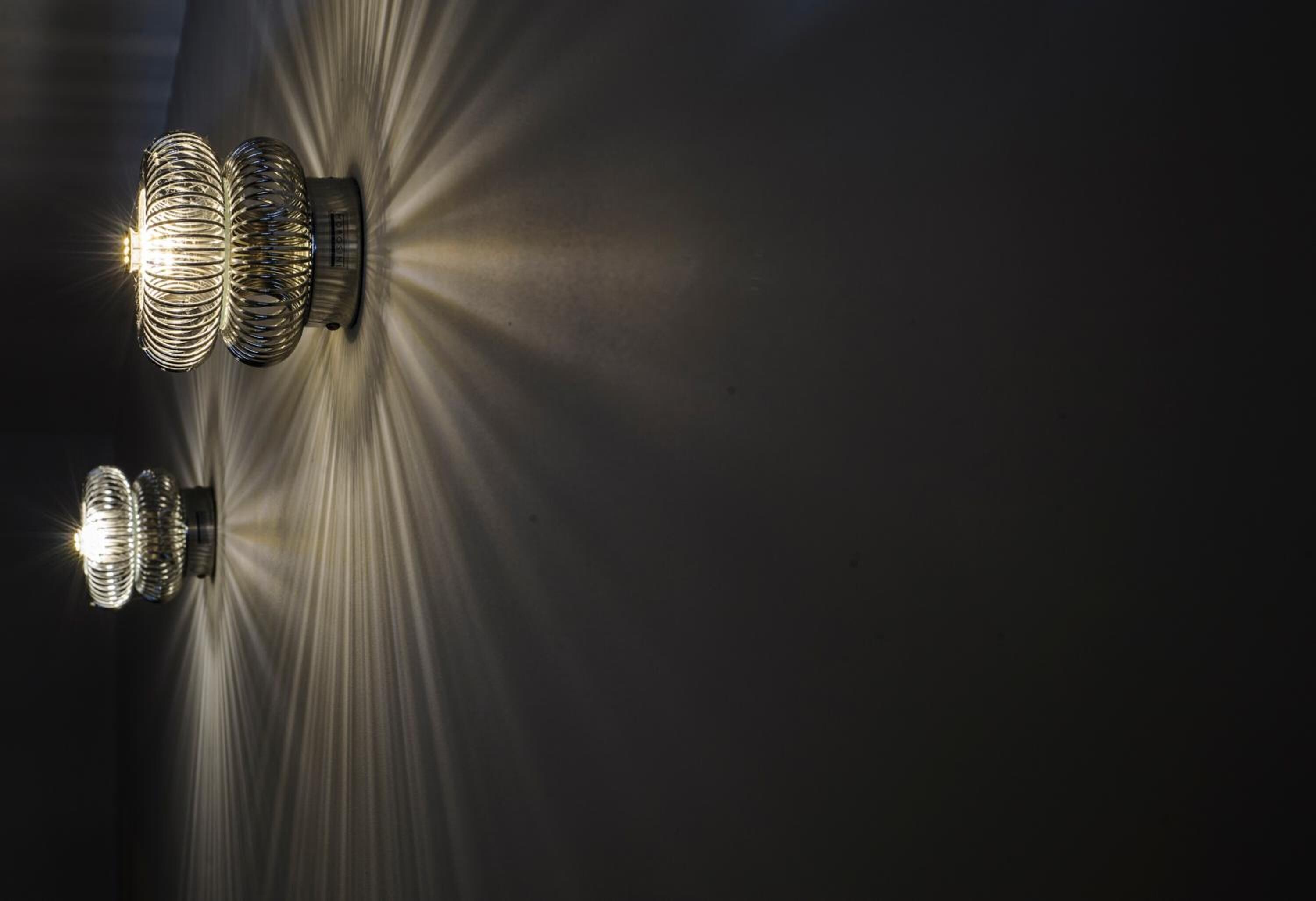Dues làmpades de paret amb disseny espiral que il·luminen una superfície fosca.