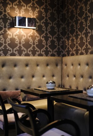 A room with a tufted sofa, a table with a bowl and a book, and a wall-mounted light fixture. - The Hide London (London)