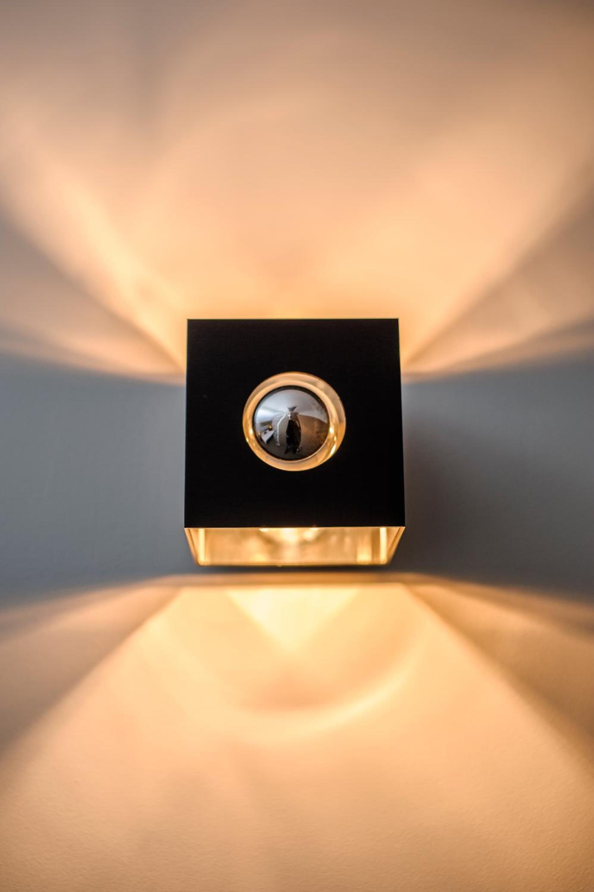 Un objeto negro cuadrado con una superficie reflectante circular, posiblemente un espejo o un adorno decorativo, sobre una superficie brillante con un brillo cálido.