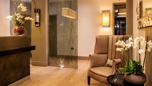 Un espace d’accueil avec un mur en marbre, un comptoir de réception, un fauteuil en cuir et un pot d’orchidée.