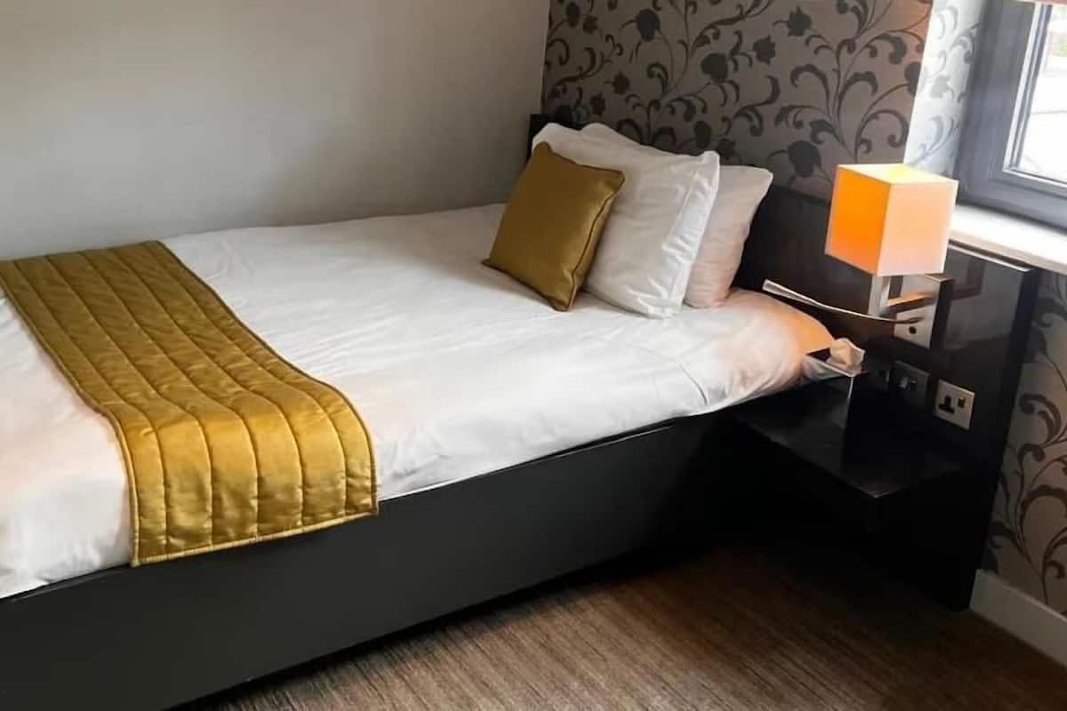 A single bed with a gold accent, white pillows, and a black nightstand with a lamp.