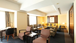 A hotel room with a living area featuring a sofa set, a coffee table, and a desk with a chair.