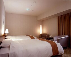 A hotel room with two beds, a chair, a small table, and a large window.