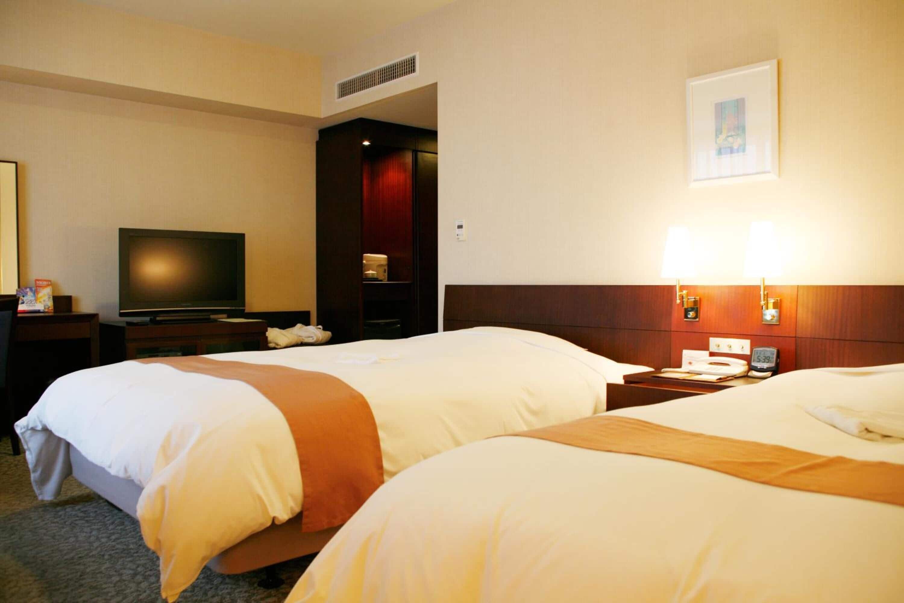 A hotel room with two beds, a television, a desk, and a nightstand.
