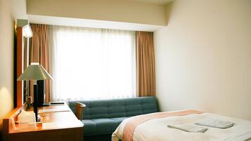 Une chambre d’hôtel avec un lit, un bureau avec une lampe, un canapé et une fenêtre avec des rideaux.