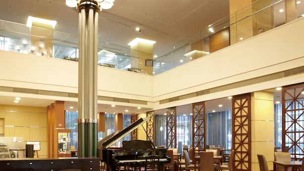 A spacious lobby with a grand piano, comfortable seating, a large chandelier, and a modern design.