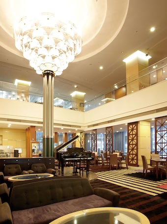 A spacious lobby with a grand piano, comfortable seating, a large chandelier, and a modern design.