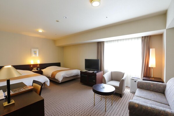 A hotel room with two beds, a desk, a chair, a sofa, a TV, and a small table.