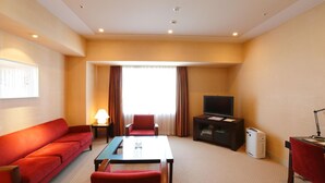 A hotel room with a red sofa, a small table, a TV, and a heater.