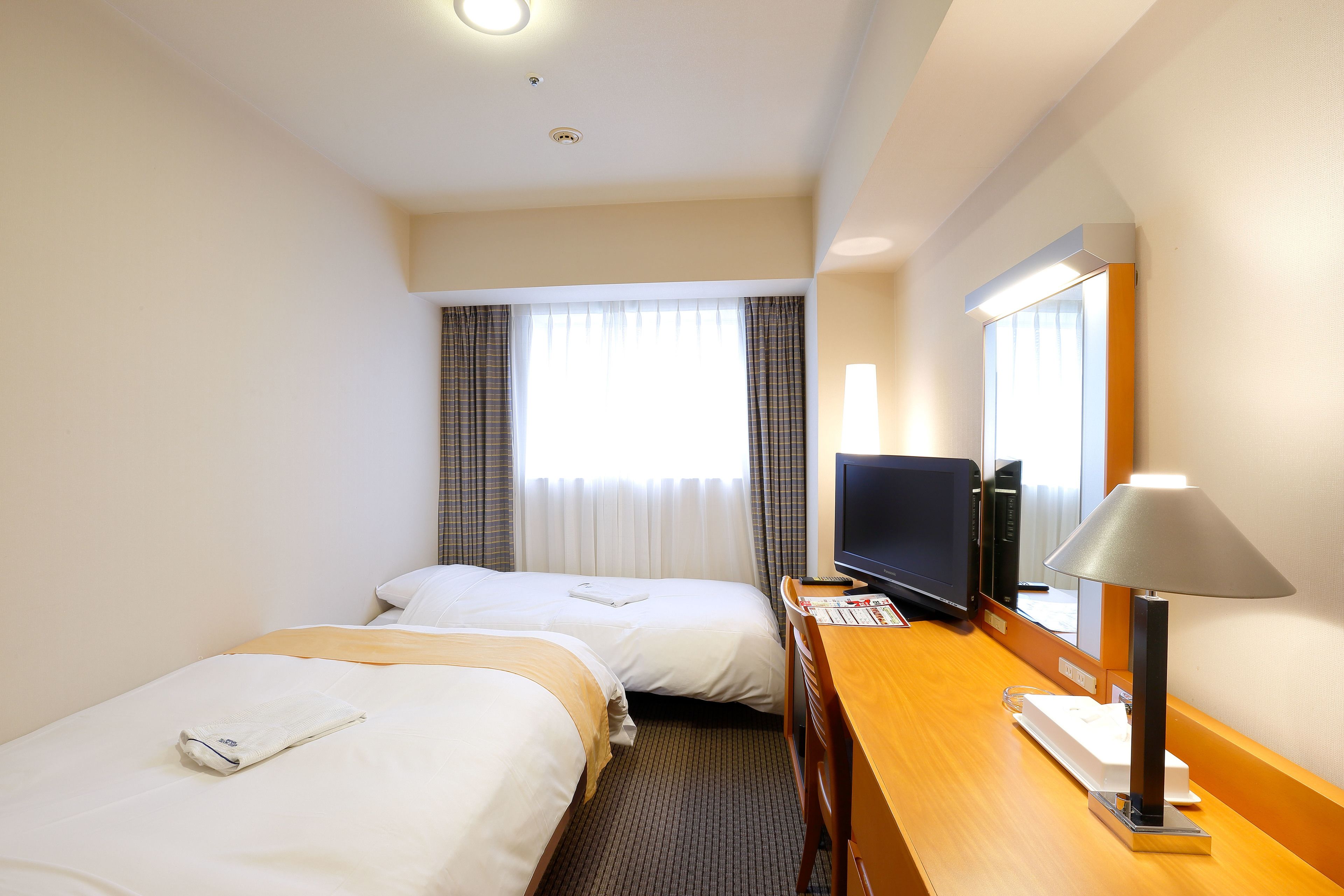 Une chambre d’hôtel avec deux lits, un bureau avec une lampe, une télévision et une fenêtre avec des rideaux.
