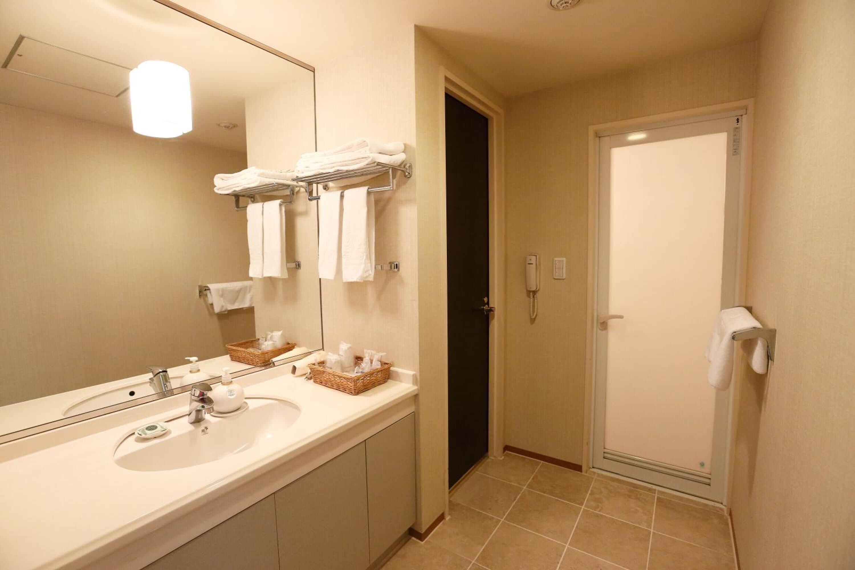A hotel bathroom with a sink, mirror, towel rack, and a shower door.