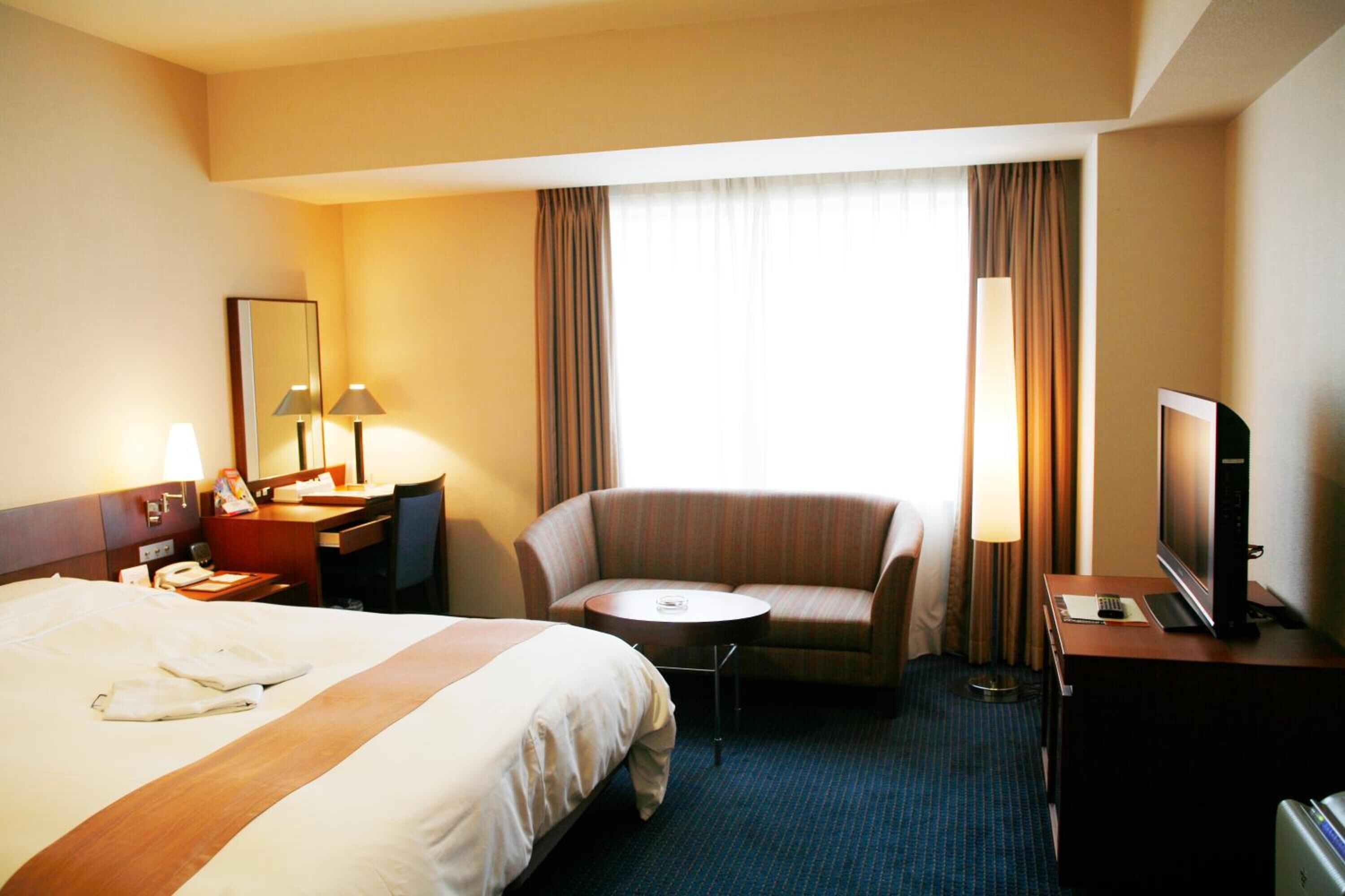 Une chambre d’hôtel avec un grand lit, un bureau, une chaise, une télévision et une fenêtre avec des rideaux.