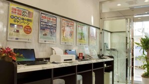 Mostrador de recepción con computadora, impresora y teléfono. Hay carteles promocionales en la pared.