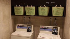Un cuarto de lavandería con dos máquinas y cuatro bolsas verdes con la etiqueta 'Laundry' en la pared.