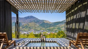 A wooden deck with a hot tub, wooden chairs, and a view of a town and mountains. - Kinnotake Sengokuhara - Adult Only (Hakone)