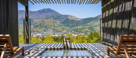 A wooden deck with a hot tub, wooden chairs, and a view of a town and mountains.