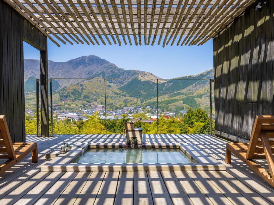 A wooden deck with a hot tub, wooden chairs, and a view of a town and mountains.